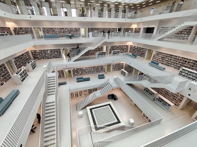 fotografia interna da biblioteca de Stuttgart, na Alemanhã. A foto mostra um ambiente predominantemente branco, com muitas escadas e livros em prateleiras